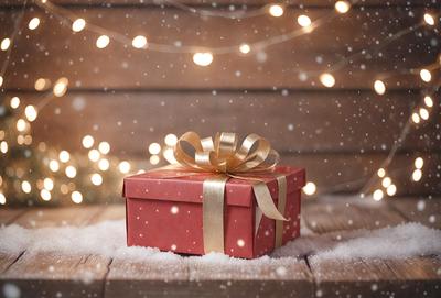 The primary subject of the image is a red box with a gold bow, sitting on a wooden table. The setting is a snowy environment, with snow falling around the box. The visual style is a photo, capturing the details of the box and the snowy background. The colors and mood of the image are dominated by the red box and the snow, creating a warm and cozy atmosphere.